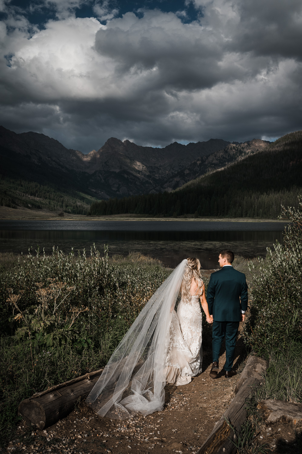 Bride and Groom walk hand in hand down path toward Piney Lake in Colorado
